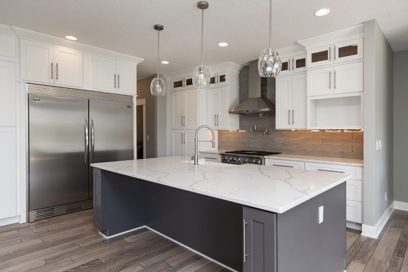 Modern kitchen with white cabinetry, stainless steel appliances, and a central island with a marble countertop.